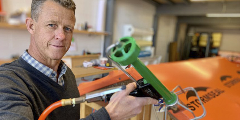 Matthew Lennox holds a green Stormseal tool in front of an orange roof prototype