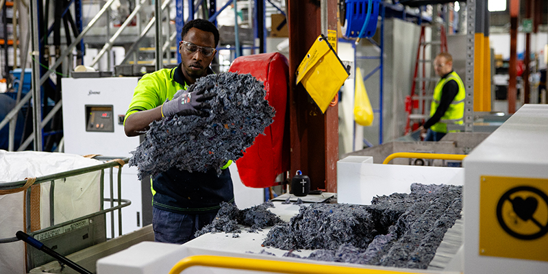 Male BlockTexx employee sorts through recyclable materials, he is in a factory setting and is wearing hi-vis.