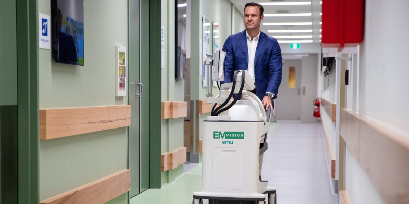 Medical professional pushes medical device on wheels through hospital hallway