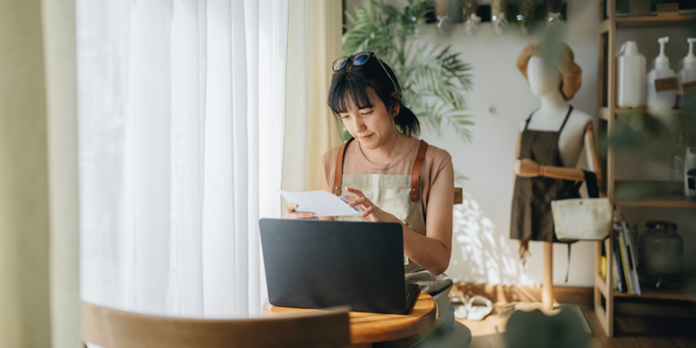 Woman reading a letter while using a laptop. 