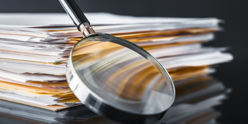 Legislative changes - magnifying glass leaning against a stack of papers and manila folders with a dark black background