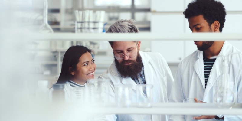 one female and two male professional scientists are in the lab, all wearing white conducting an experiment