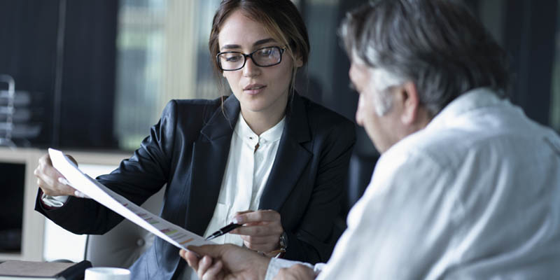 A businesswoman speaking with a businessman. They are looking at documents about trade marks or other business dealings. 